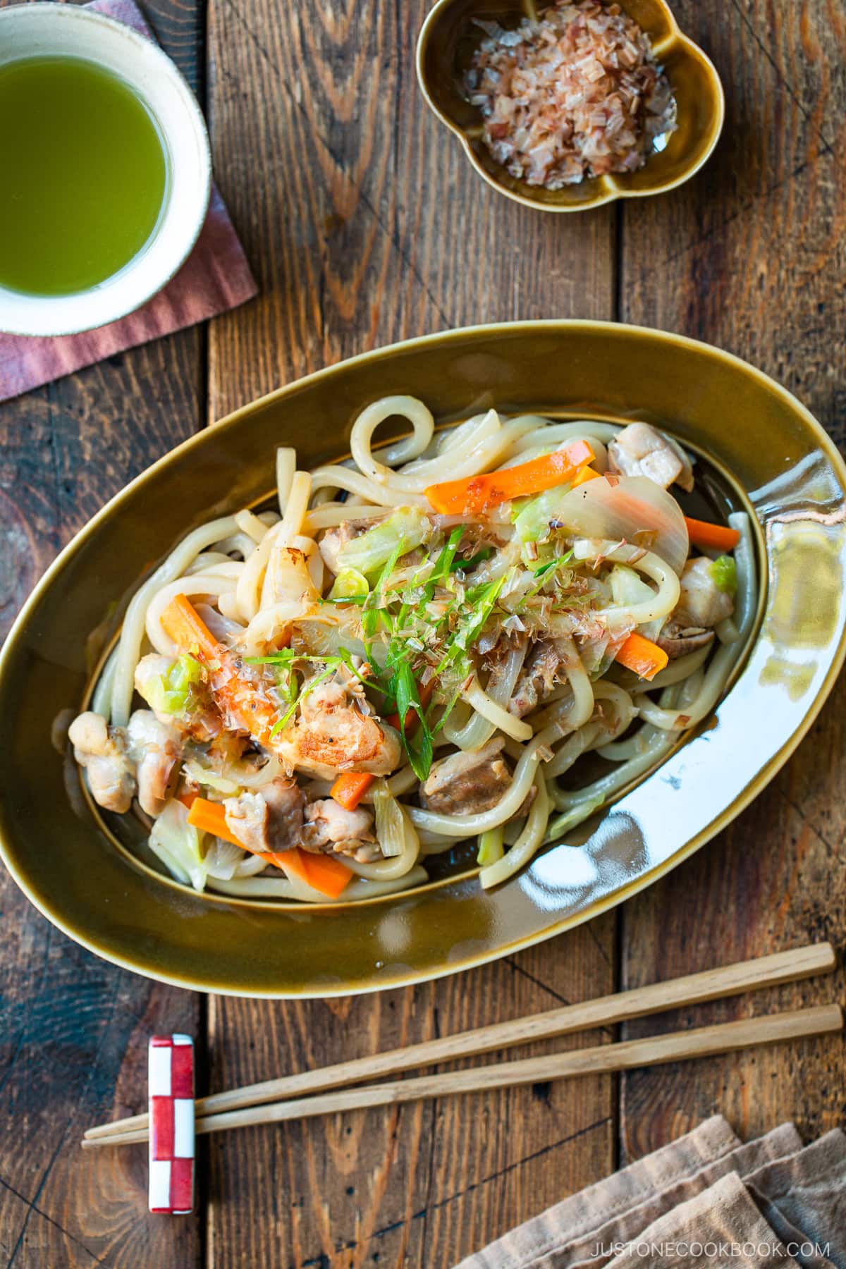 An olive colored oval plate containing Yaki Udon, Japanese stir-fried udon noodles with chicken and vegetables.