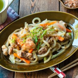 An olive colored oval plate containing Yaki Udon, Japanese stir-fried udon noodles with chicken and vegetables.