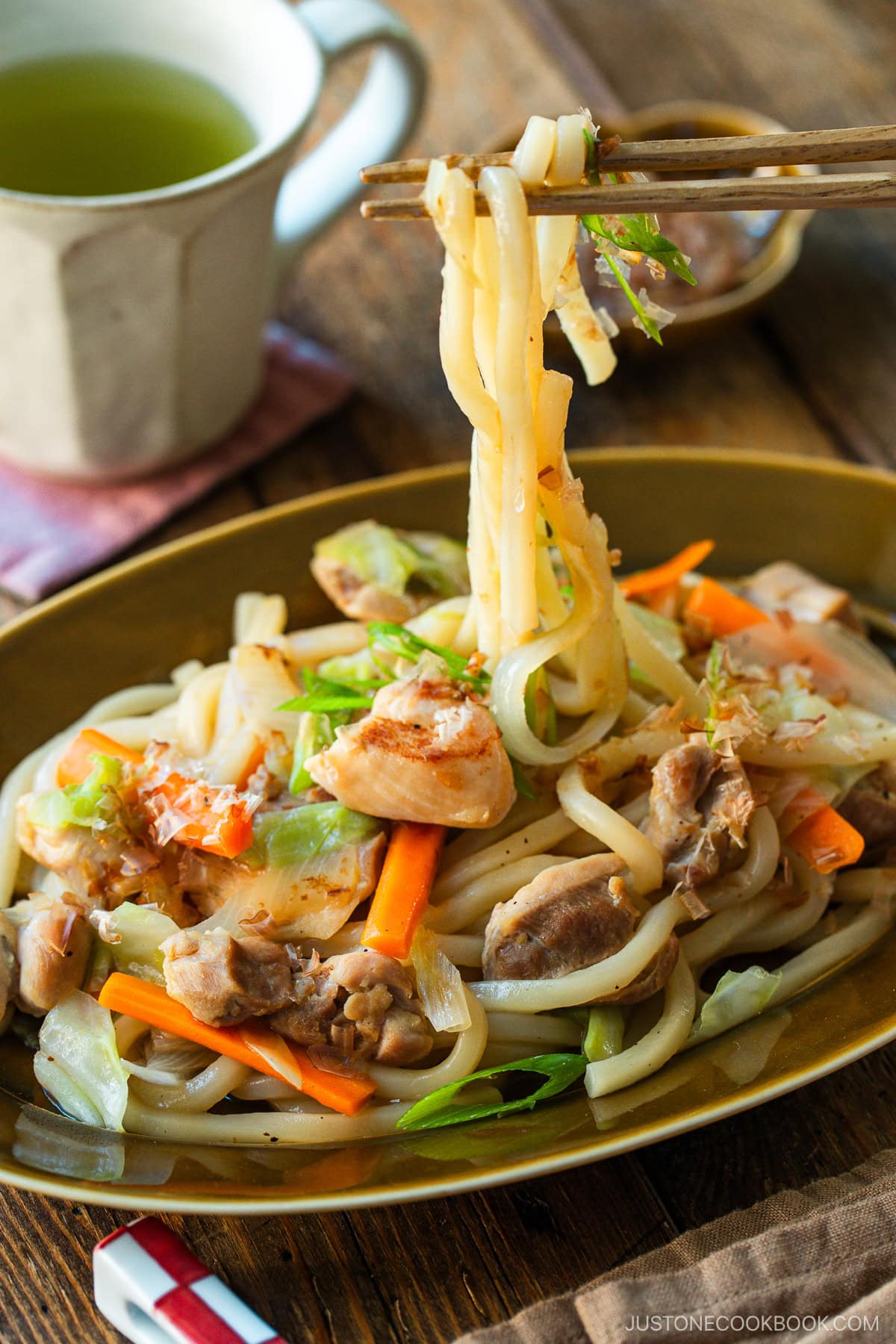 An olive colored oval plate containing Yaki Udon, Japanese stir-fried udon noodles with chicken and vegetables.