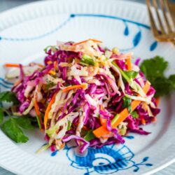 Asian Coleslaw with Sesame Dressing on a white plate along with gold fork and knife.