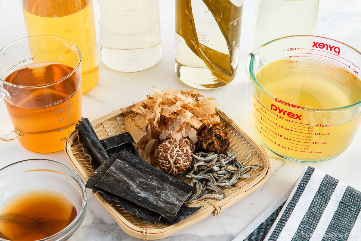 Kombu, Shiitake mushrooms, Katsuobushi, and Iriko are on a bamboo tray, beside cups of dashi. stock.