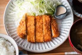 A Japanese ceramic plate containing Tonkatsu (pork cutlet) and shredded cabbage salad.