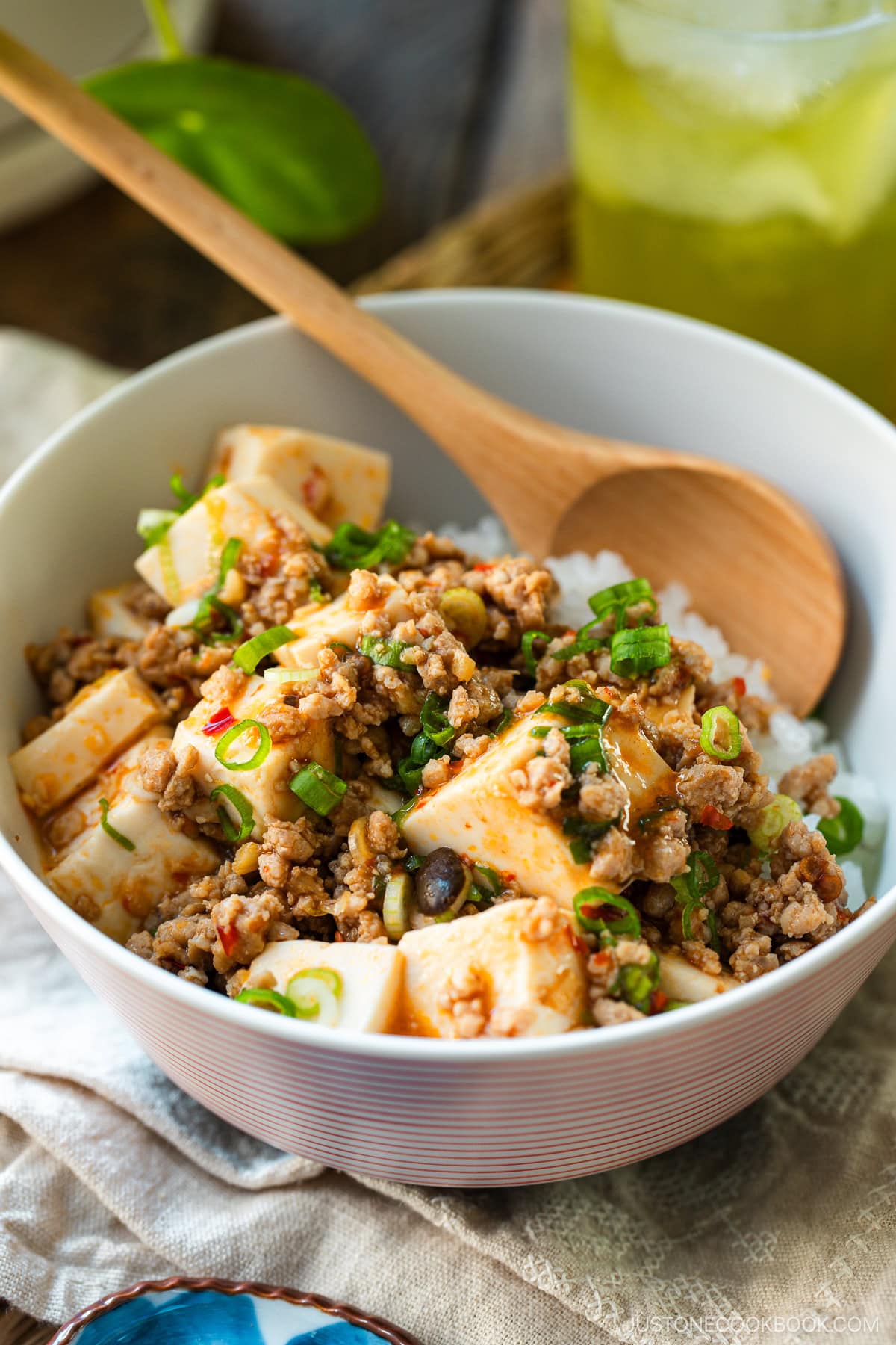 A donburi bowl containing mapo tofu over bed of steamed rice, served with a glass of green tea.