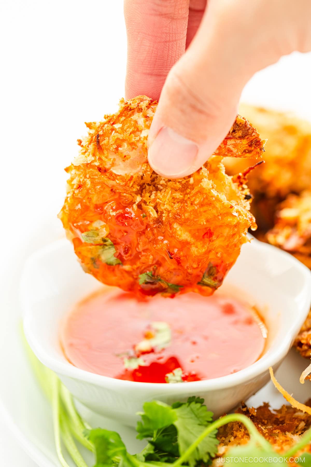 Coconut Shrimp are held over the sauce dish with fingers.