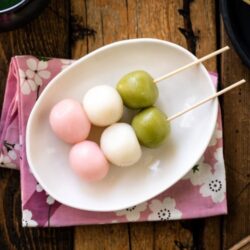 A white oval plate containing two Hanami Dango, served with matcha green tea.