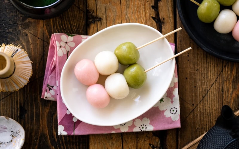 A white oval plate containing two Hanami Dango, served with matcha green tea.