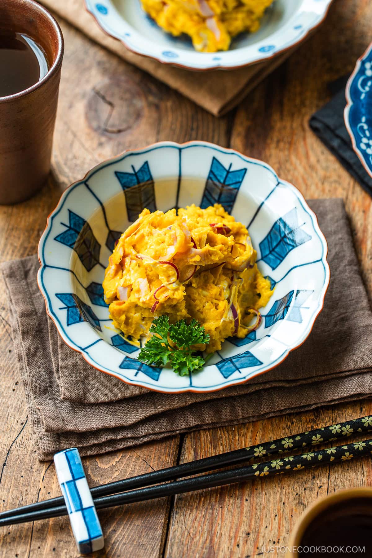 A Japanese round plate containing velvety and rich Kabocha Salad with crisp and refreshing red onion slices and ham, mixed with cream cheese and tangy Japanese mayo.