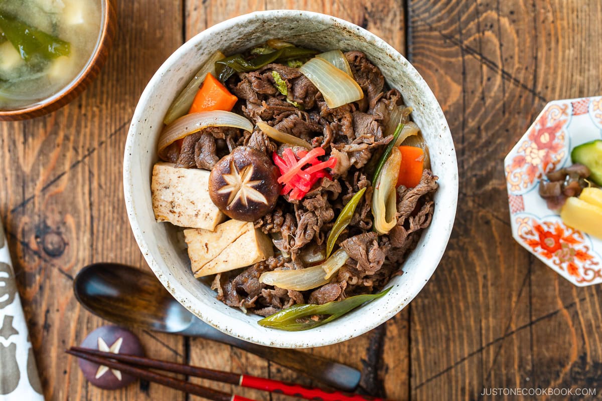 A large ceramic donburi rice bowl containing Sukiyaki Don, thinly sliced beef, tofu, and vegetables simmered in a savory dashi soy broth and served over steamed rice.