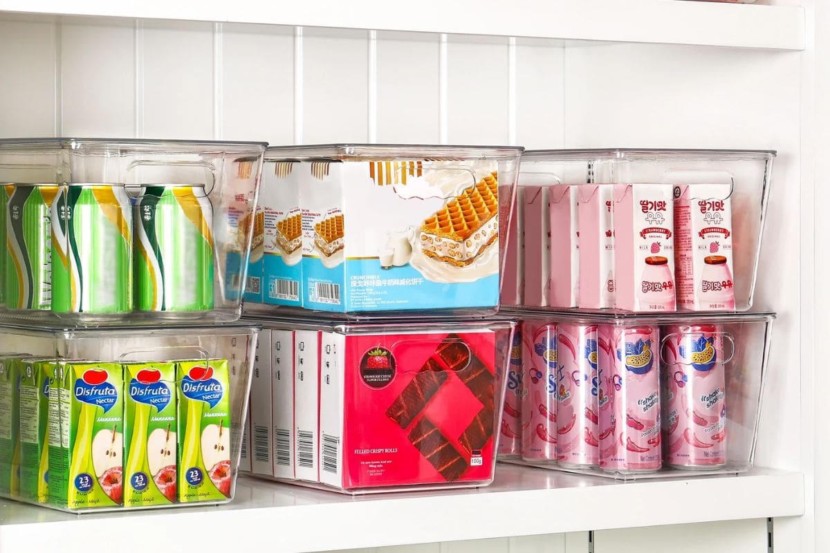 Assorted Asian beverages and snacks organized in clear storage bins inside a refrigerator or pantry shelf.