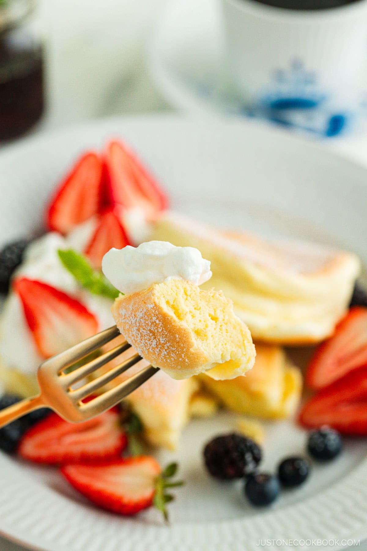 A white plate containing Japanese souffle pancakes dusted with powdered sugar, fresh mixed berries, and whipped cream.