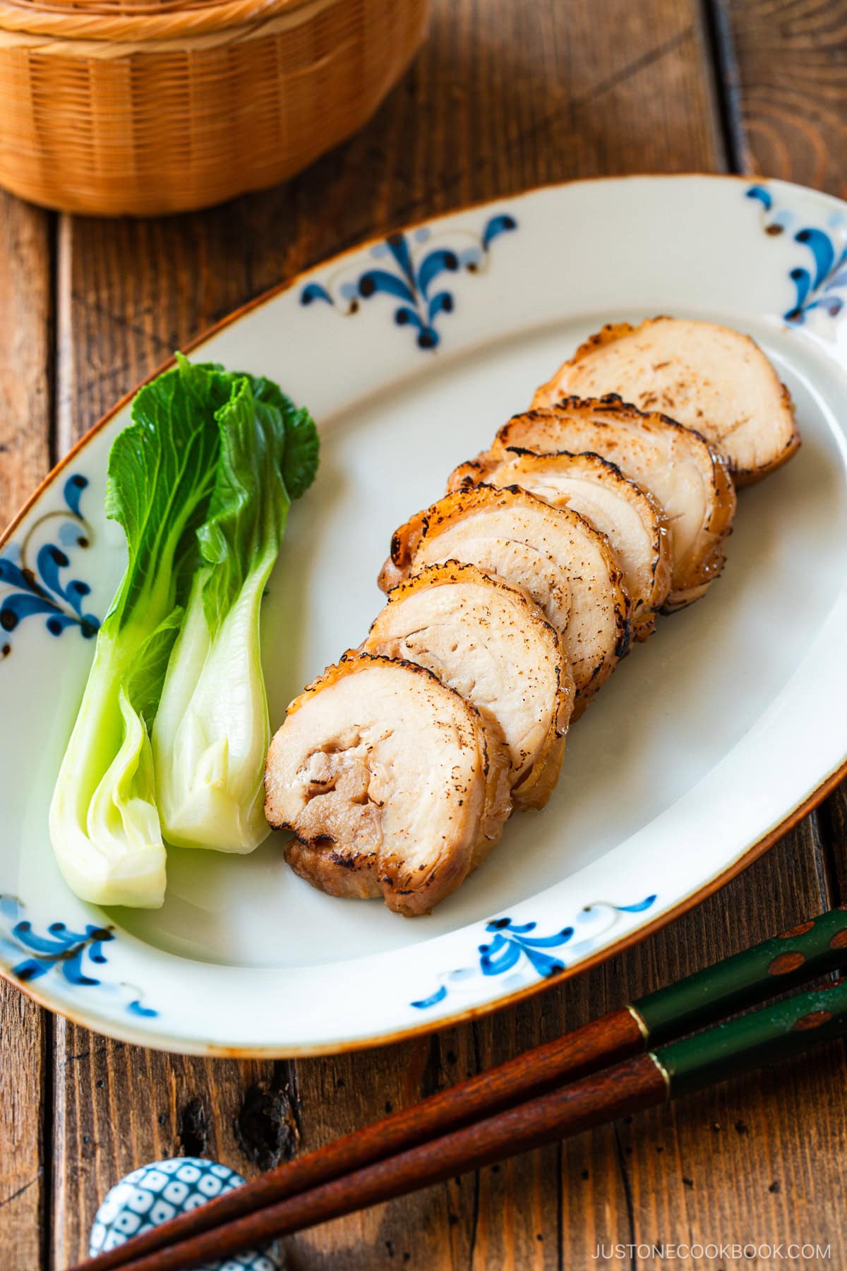 A rectangular plate containing thinly sliced, seared chicken chashu served with bok choy.