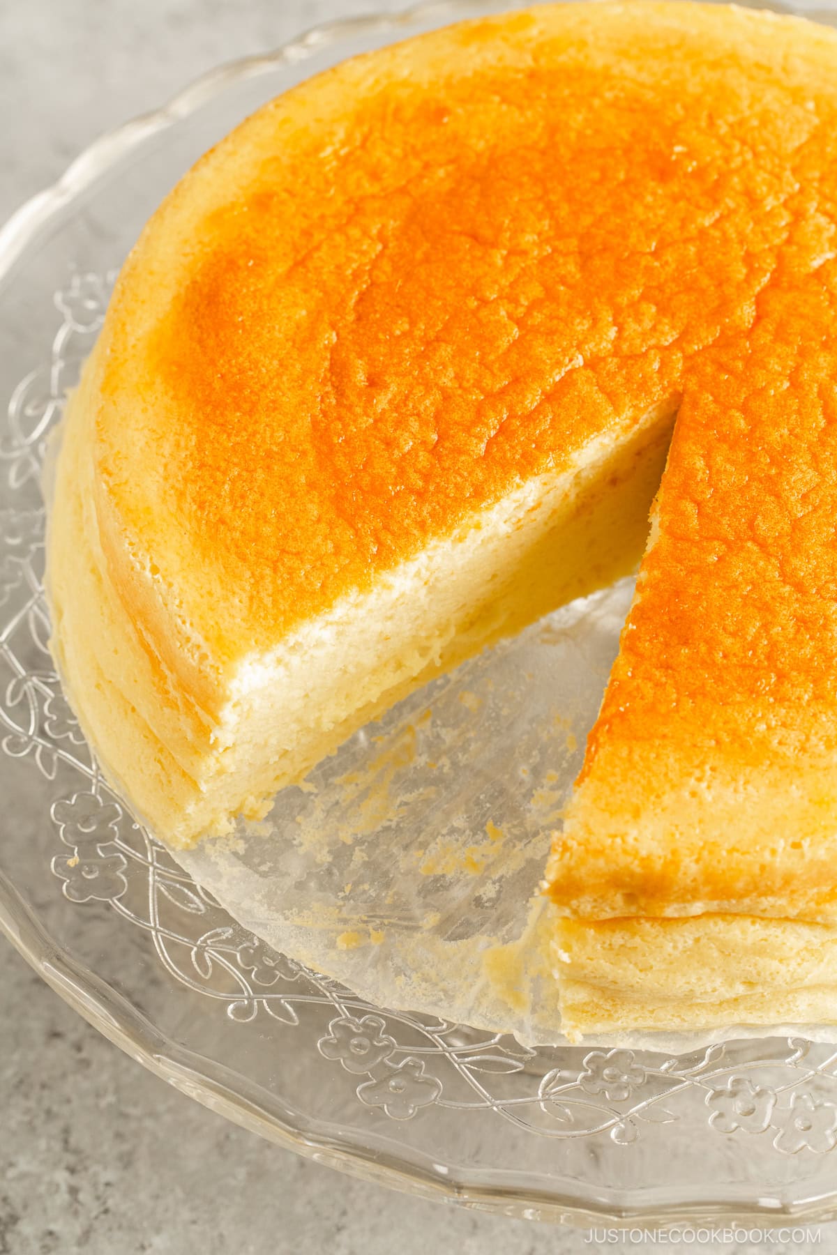 A glass cake stand containing Japanese souffle cheesecake slice being cut out.