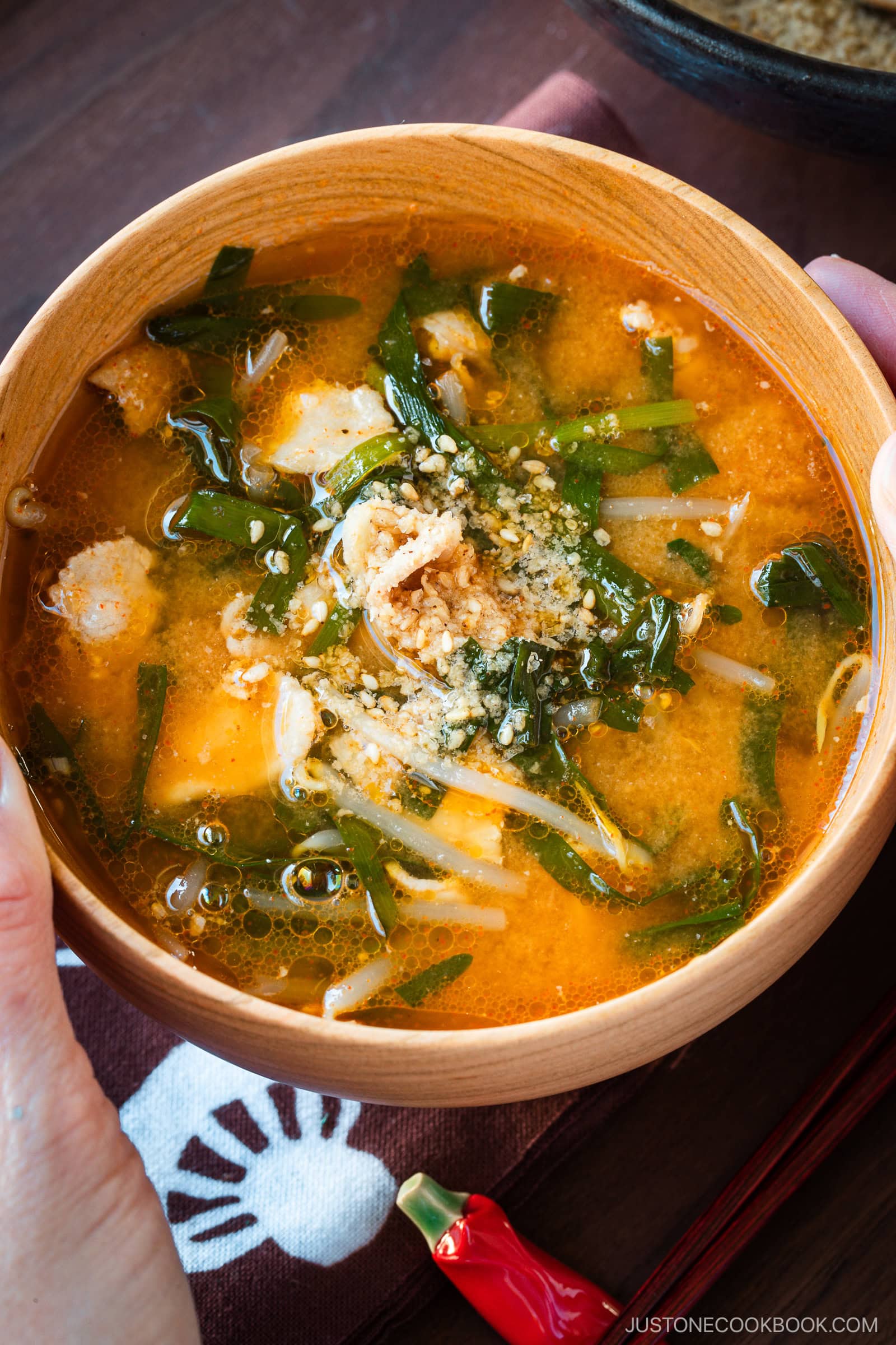 A light wooden bowl containing Spicy Pork and Bean Sprout Miso Soup sprinkled with ground sesame seeds.