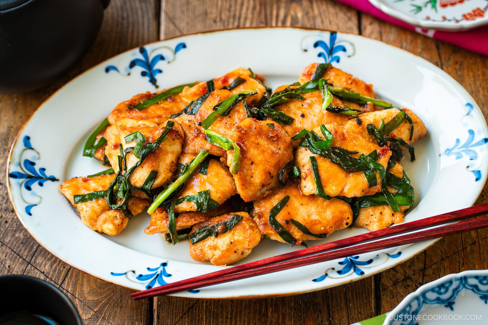 An oval plate containing Chicken Stir-fry with Garlic Chives served on the table along with tea pot and small plates.