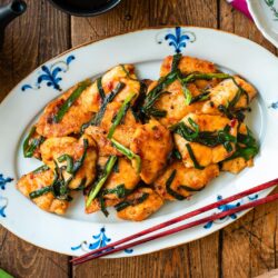 An oval plate containing Chicken Stir-fry with Garlic Chives served on the table along with tea pot and small plates.