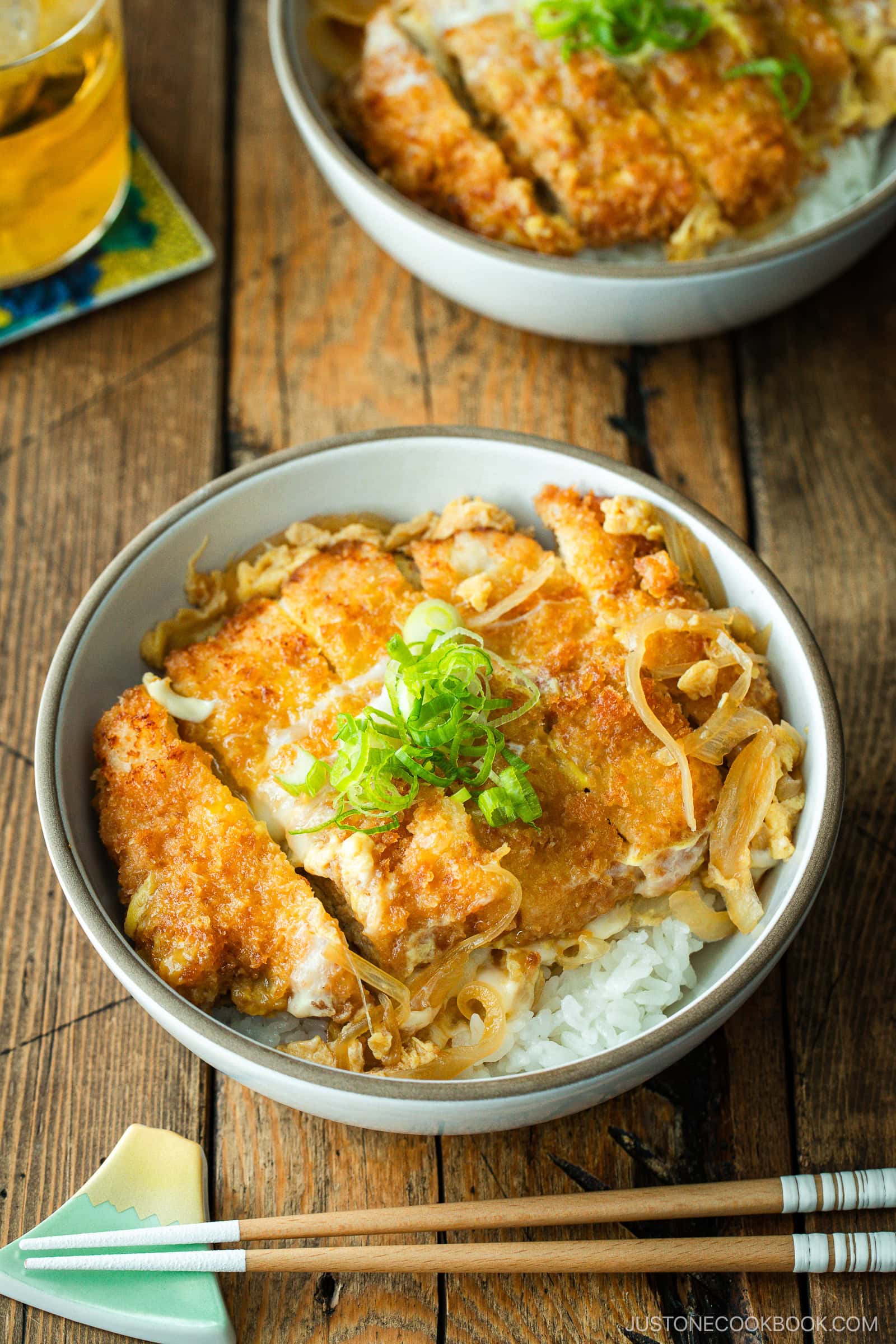 A white bowl containing Katsudon, pork cutlet rice bowl, where golden brown tonkatsu, drizzled egg, and tender onion are simmered in a savory dashi broth.
