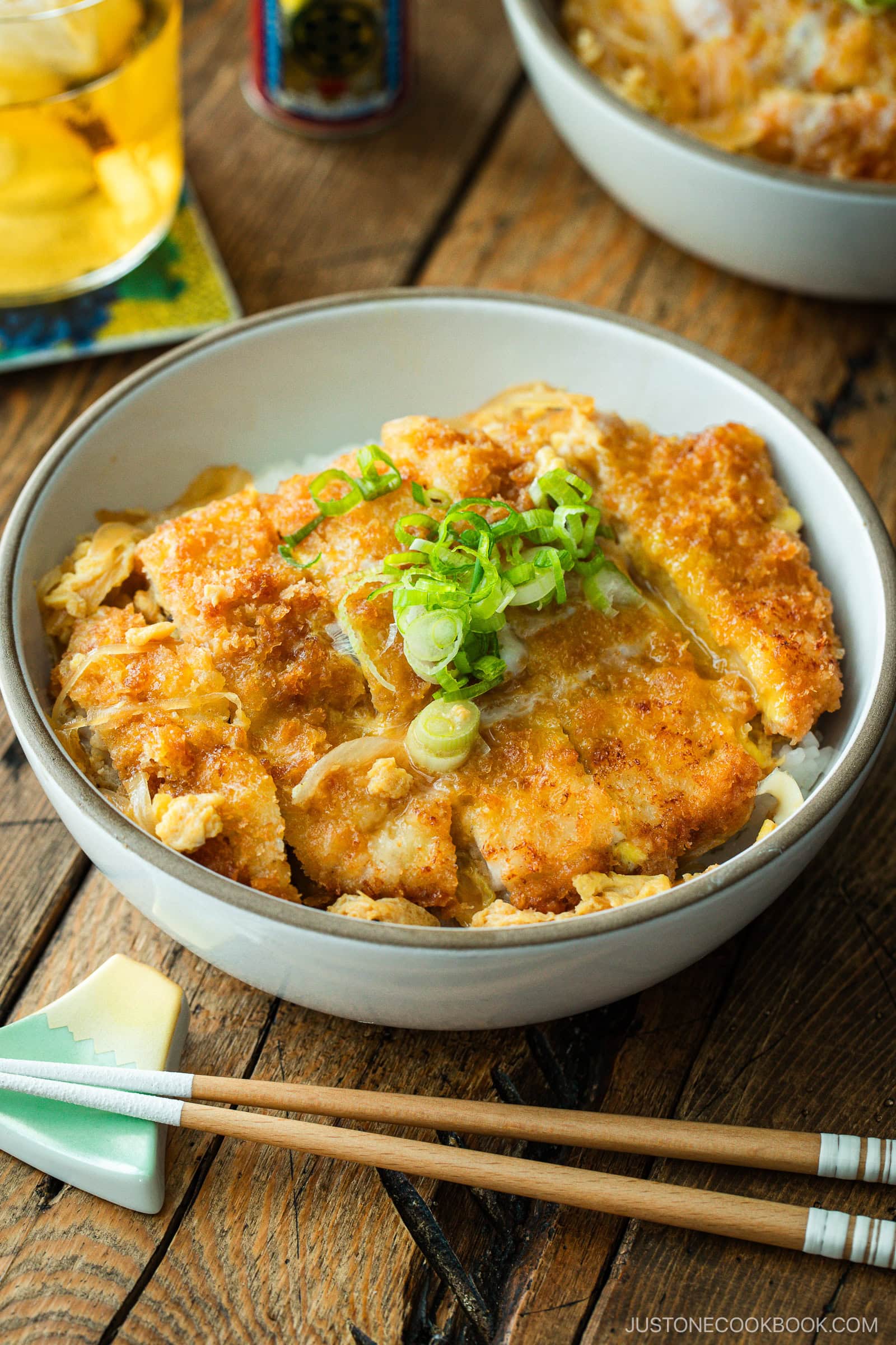 A white bowl containing Katsudon, pork cutlet rice bowl, where golden brown tonkatsu, drizzled egg, and tender onion are simmered in a savory dashi broth.