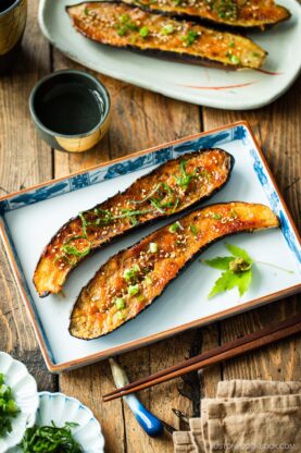 A rectangular plate containing Miso Glazed Eggplant garnished with yuzu kosho paste on a green maple leaf on the side.
