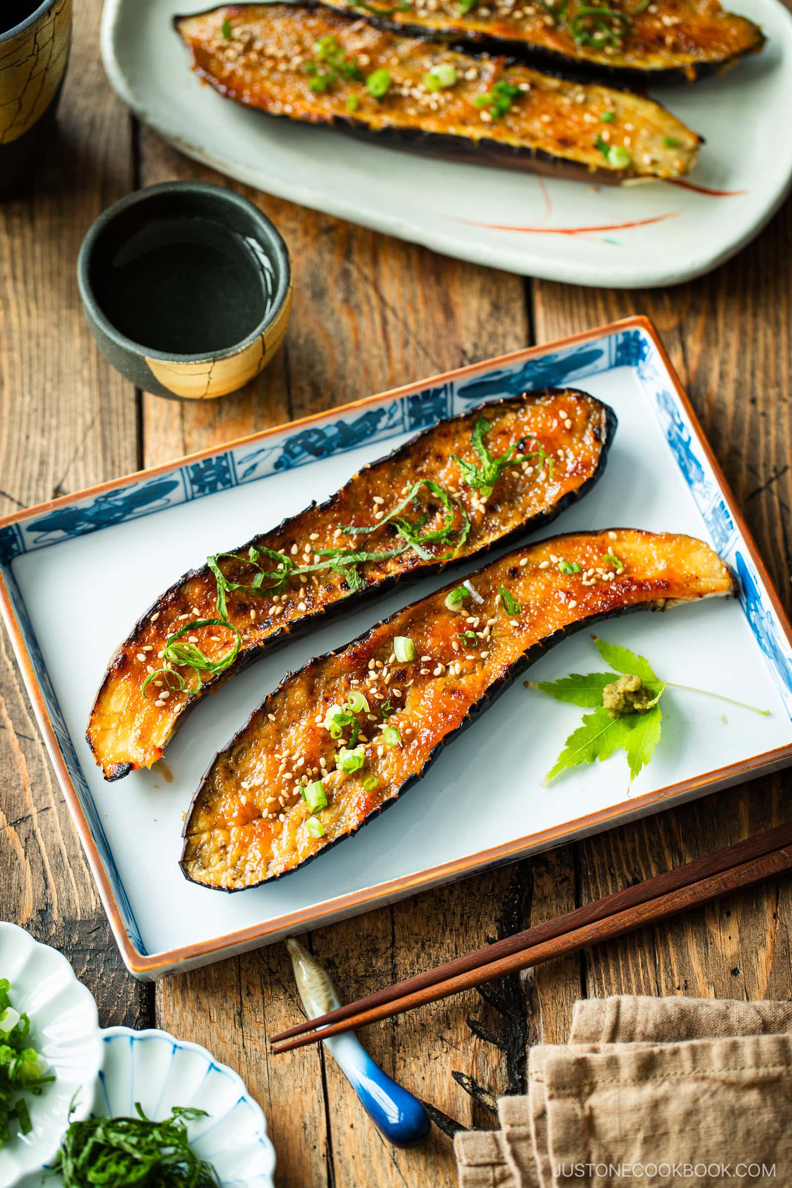 A rectangular plate containing Miso Glazed Eggplant garnished with yuzu kosho paste on a green maple leaf on the side.