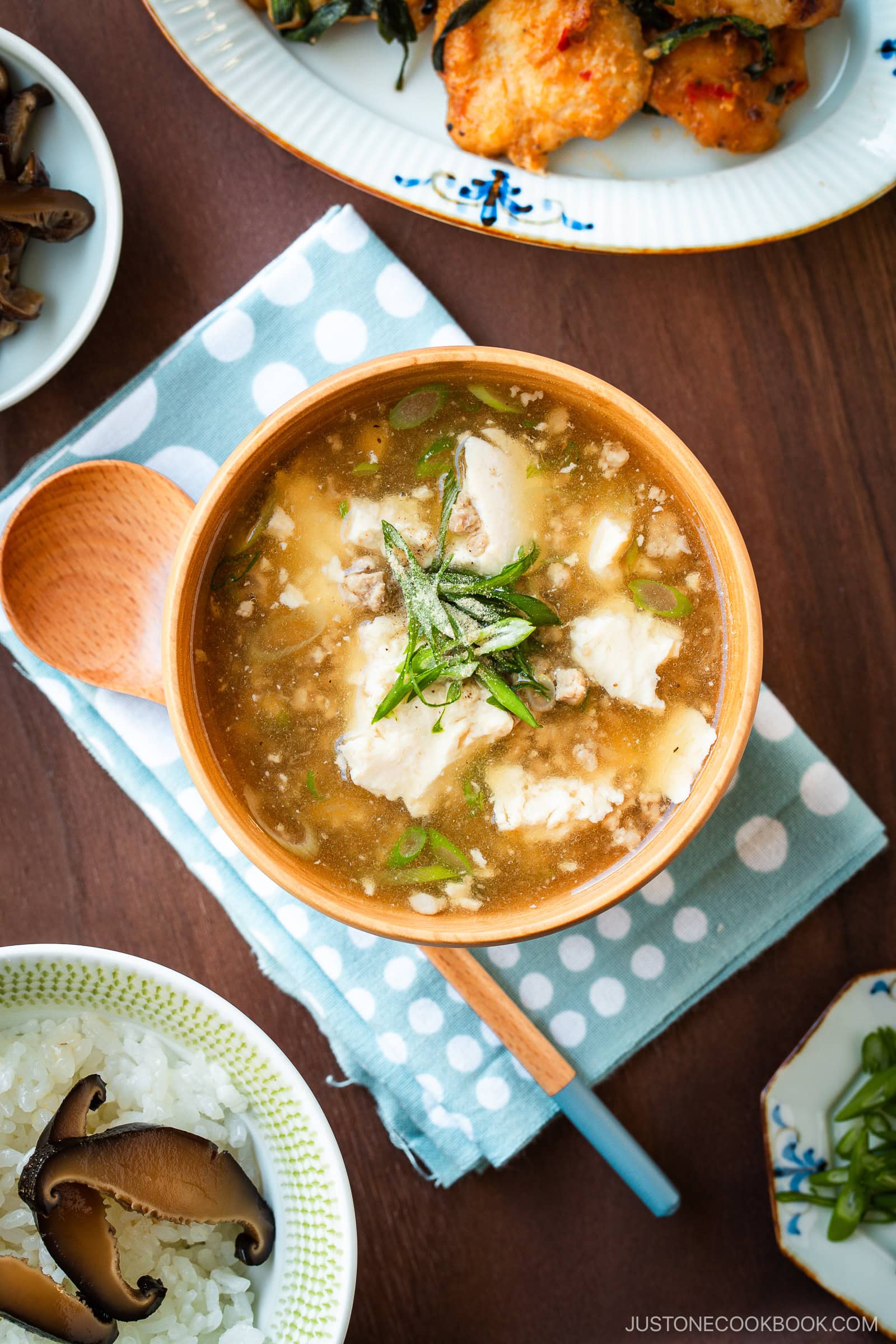 Wooden bowls filled with Pork Tofu Soup, served alongside steamed rice and a chicken dish on the table.