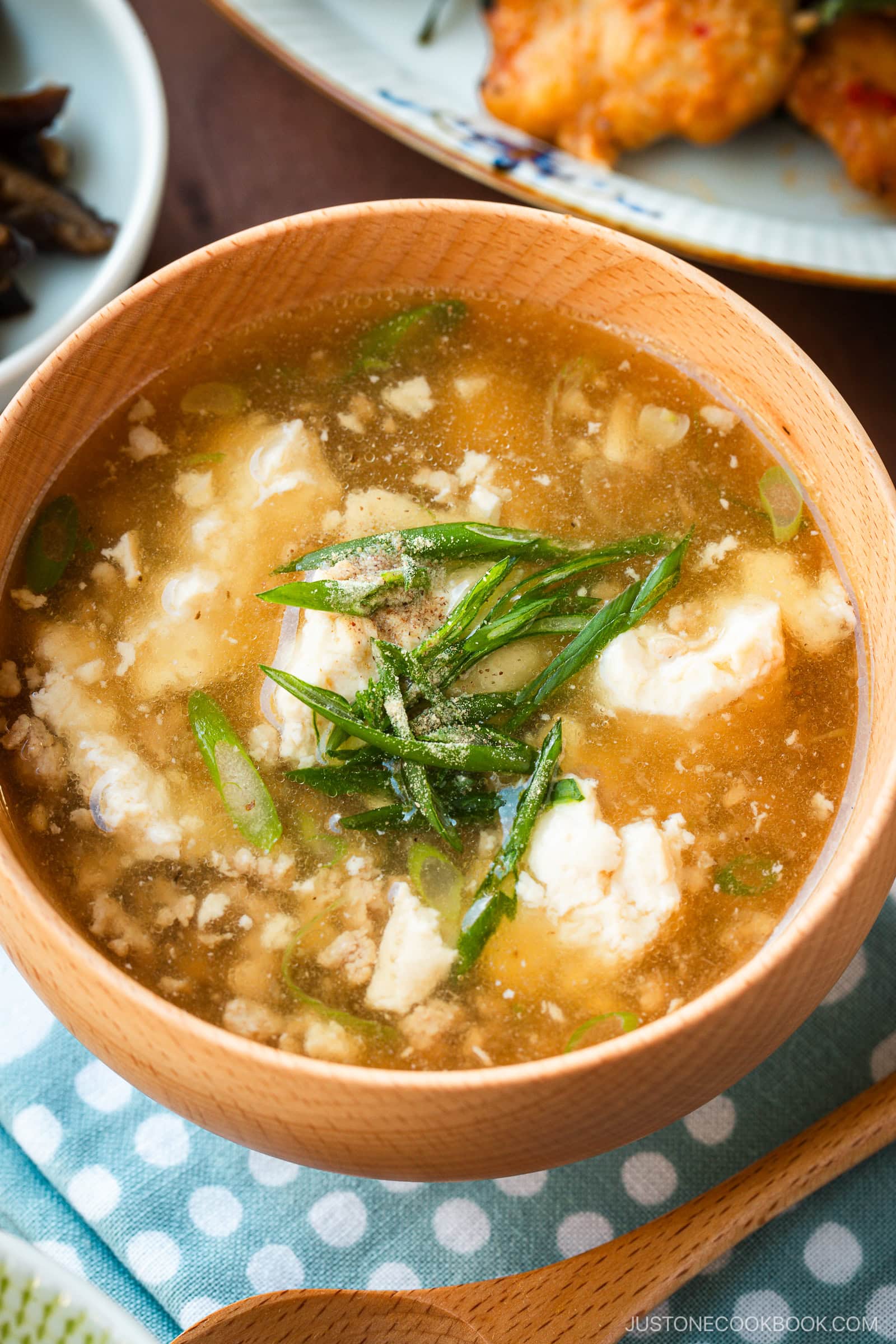 Wooden bowls filled with Pork Tofu Soup, served alongside steamed rice and a chicken dish on the table.