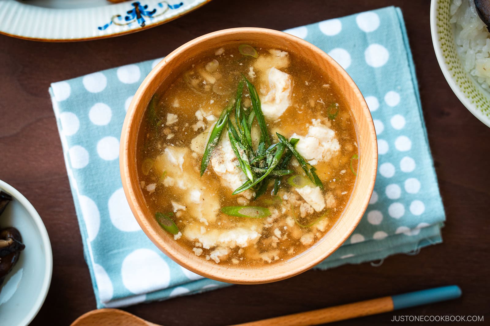 Wooden bowls filled with Pork Tofu Soup, served alongside steamed rice and a chicken dish on the table.