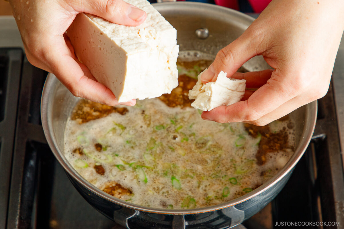 Tearing the tofu block into bite-sized pieces.