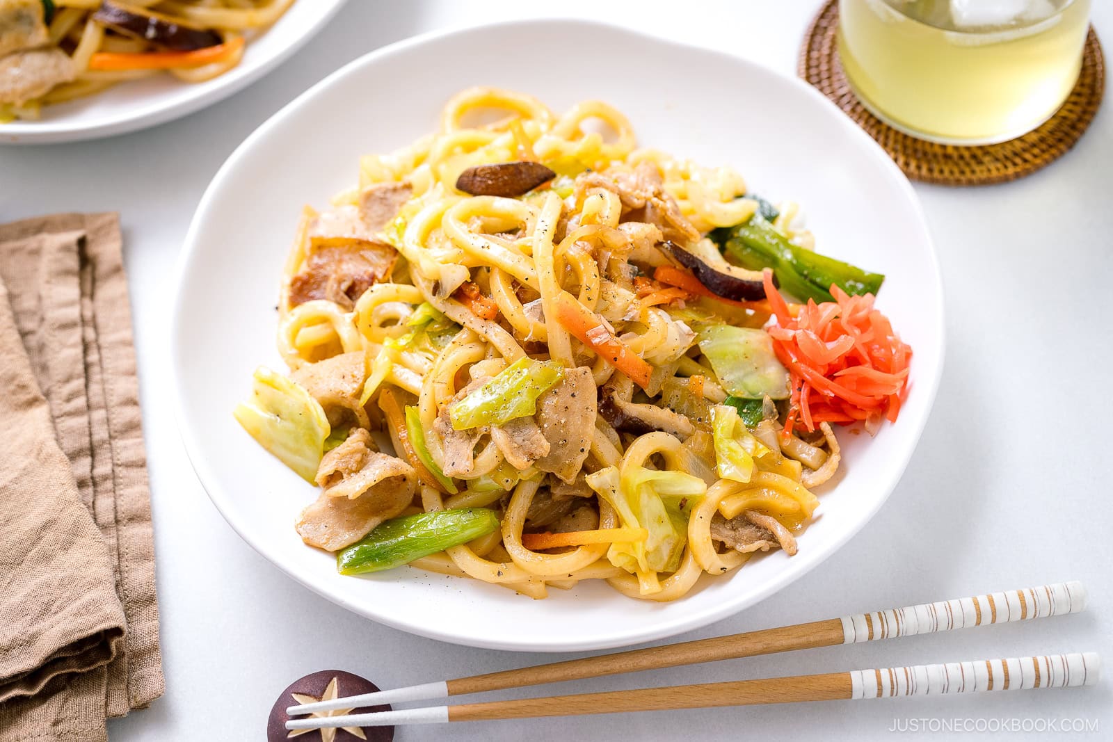 A white plate containing Yaki Udon, Japanese stir fried udon noodles with crisp vegetables and protein in a savory sauce.