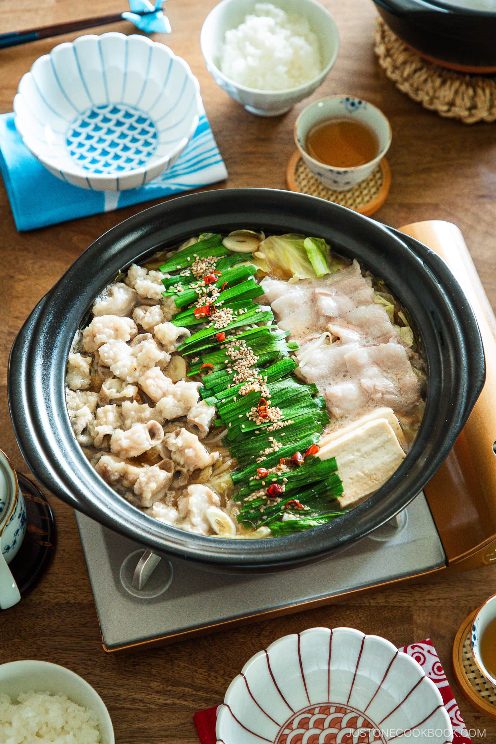 Motsunabe, a traditional Japanese hot pot featuring beef offal simmered in a flavorful broth with vegetables, is served in a donabe on a portable gas stove on the table.