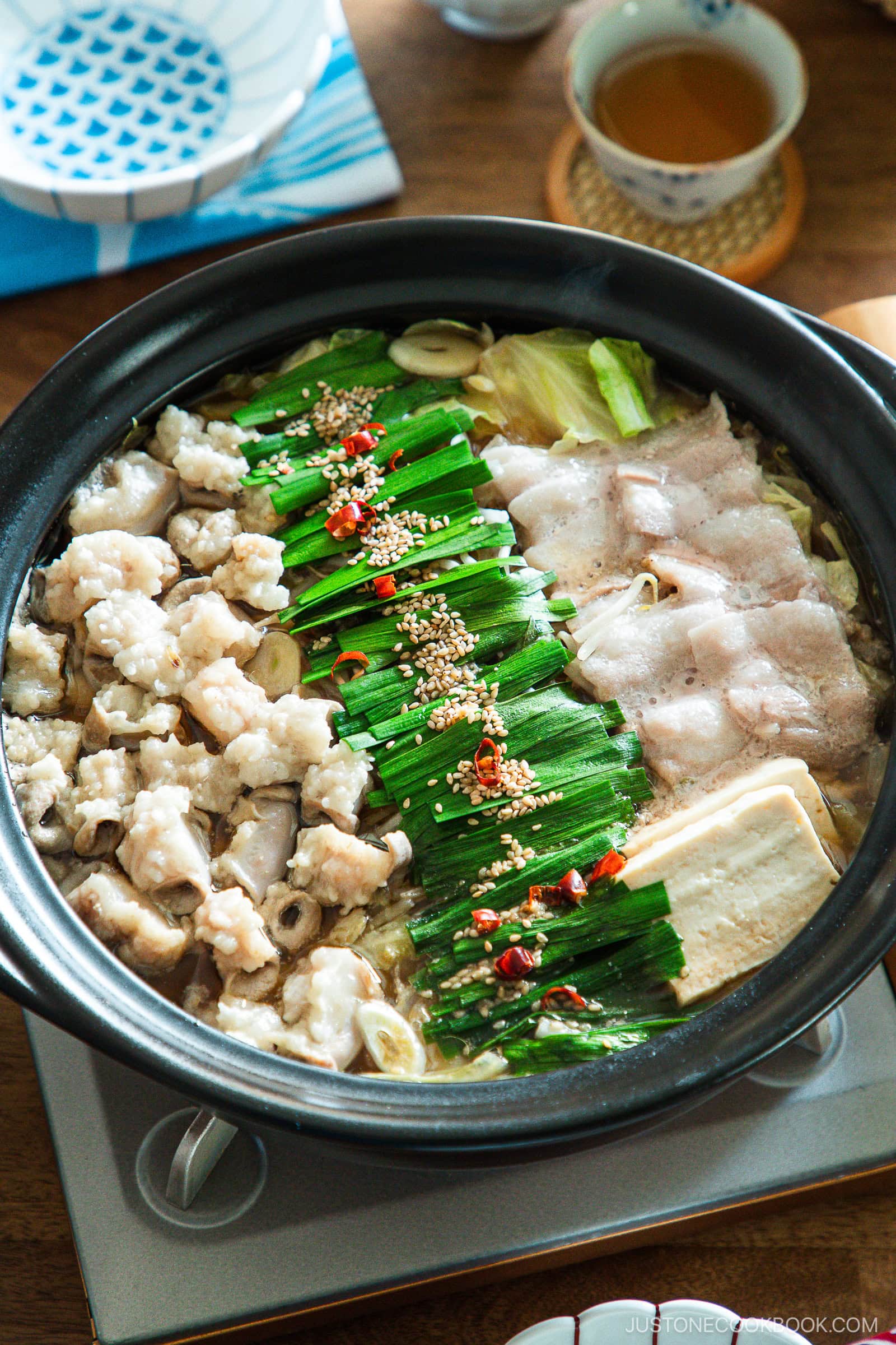 Motsunabe, a traditional Japanese hot pot featuring beef offal simmered in a flavorful broth with vegetables, is served in a donabe on a portable gas stove on the table.