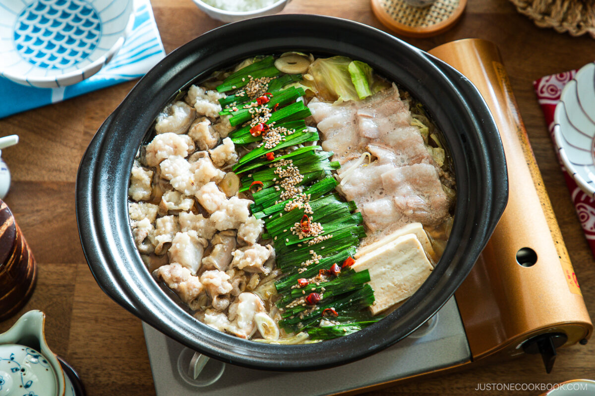 Motsunabe, a traditional Japanese hot pot featuring beef offal simmered in a flavorful broth with vegetables, is served in a donabe on a portable gas stove on the table.