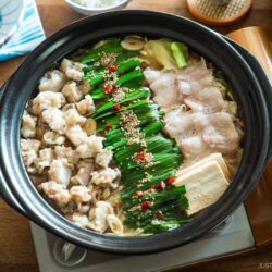 Motsunabe, a traditional Japanese hot pot featuring beef offal simmered in a flavorful broth with vegetables, is served in a donabe on a portable gas stove on the table.
