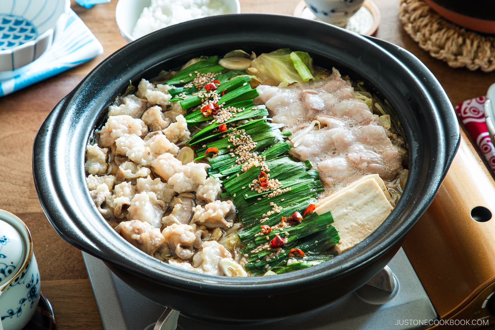 Motsunabe, a traditional Japanese hot pot featuring beef offal simmered in a flavorful broth with vegetables, is served in a donabe on a portable gas stove on the table.