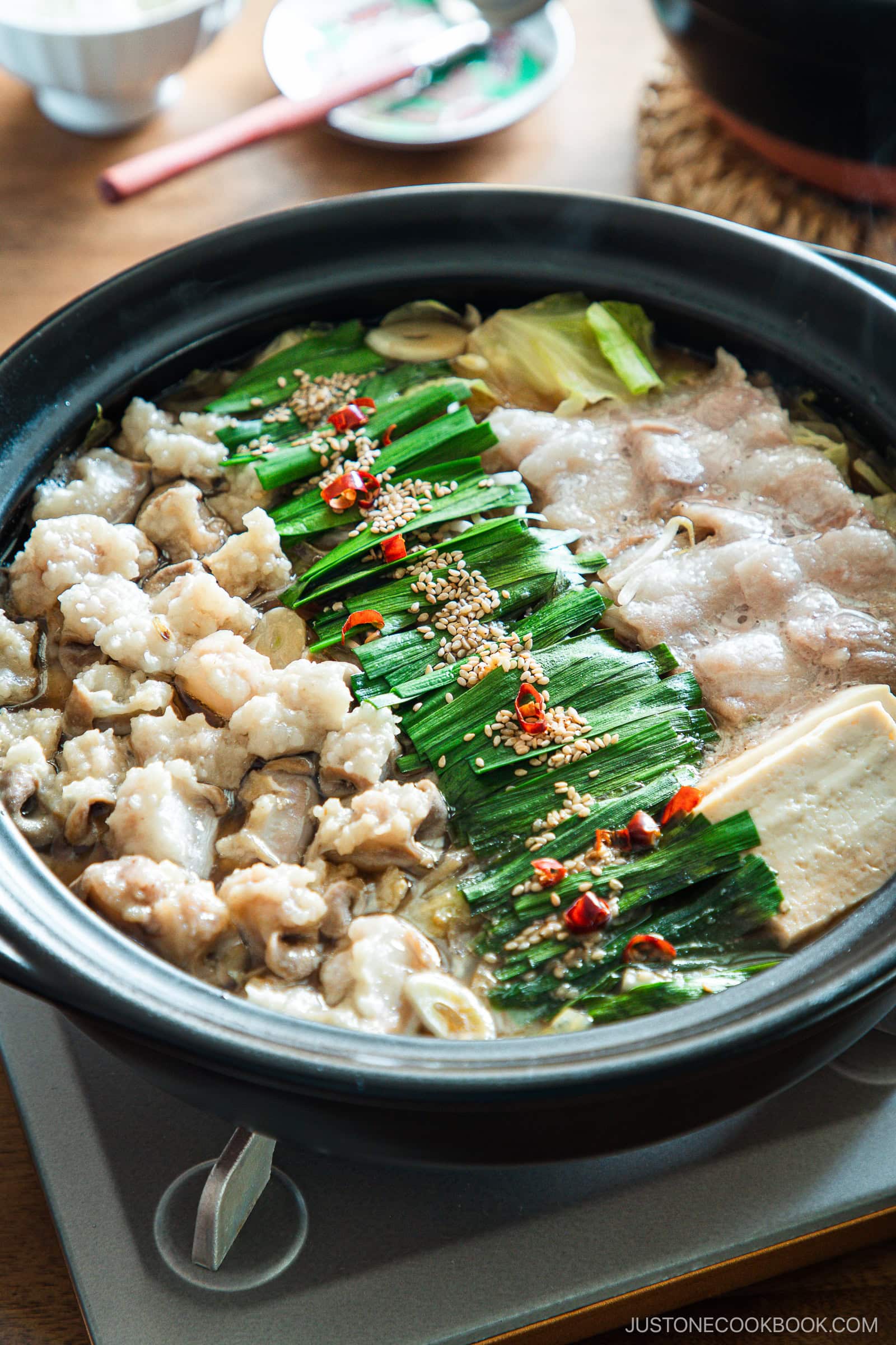 Motsunabe, a traditional Japanese hot pot featuring beef offal simmered in a flavorful broth with vegetables, is served in a donabe on a portable gas stove on the table.