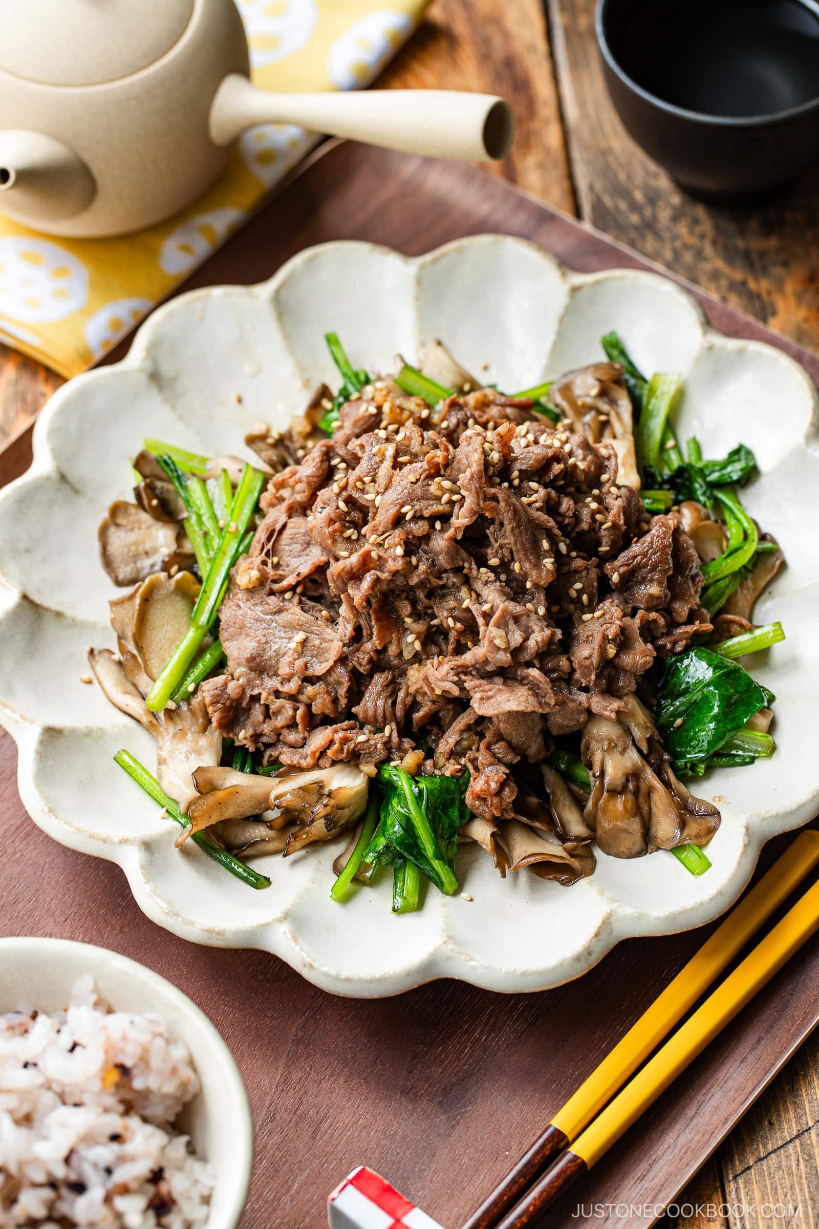 A white scalloped plate containing stir-fried Butter Ponzu beef with komatsuna green and maitake mushrooms.