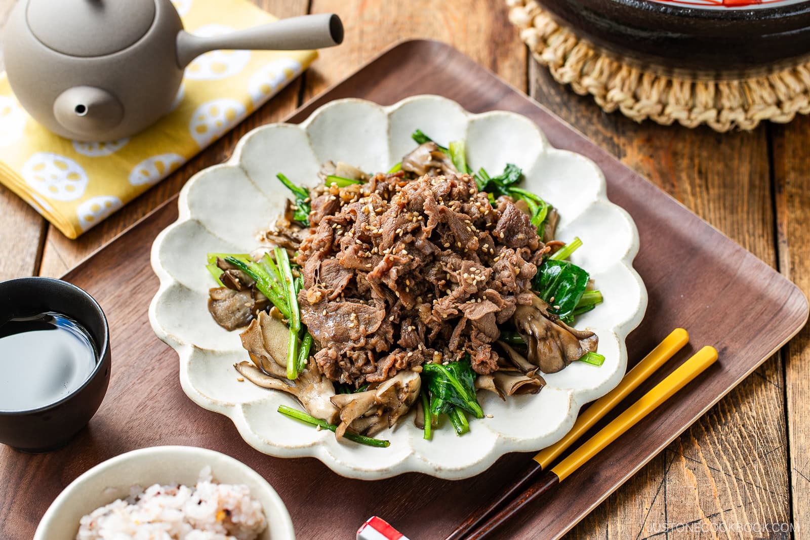 A white scalloped plate containing stir-fried Butter Ponzu beef with komatsuna green and maitake mushrooms.