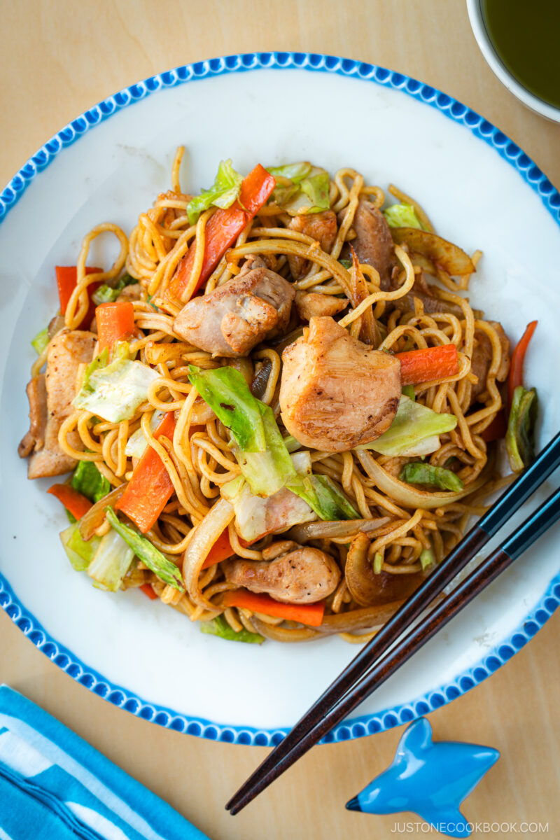 Delicious Chicken Yakisoba with tender, moist chicken thighs and crisp veggies in a sweet savory sauce plated on a beautiful white plate with blue scalloped edge.