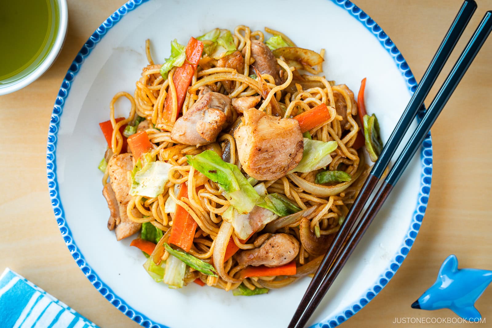 Delicious Chicken Yakisoba with tender, moist chicken thighs and crisp veggies in a sweet savory sauce plated on a beautiful white plate with blue scalloped edge.