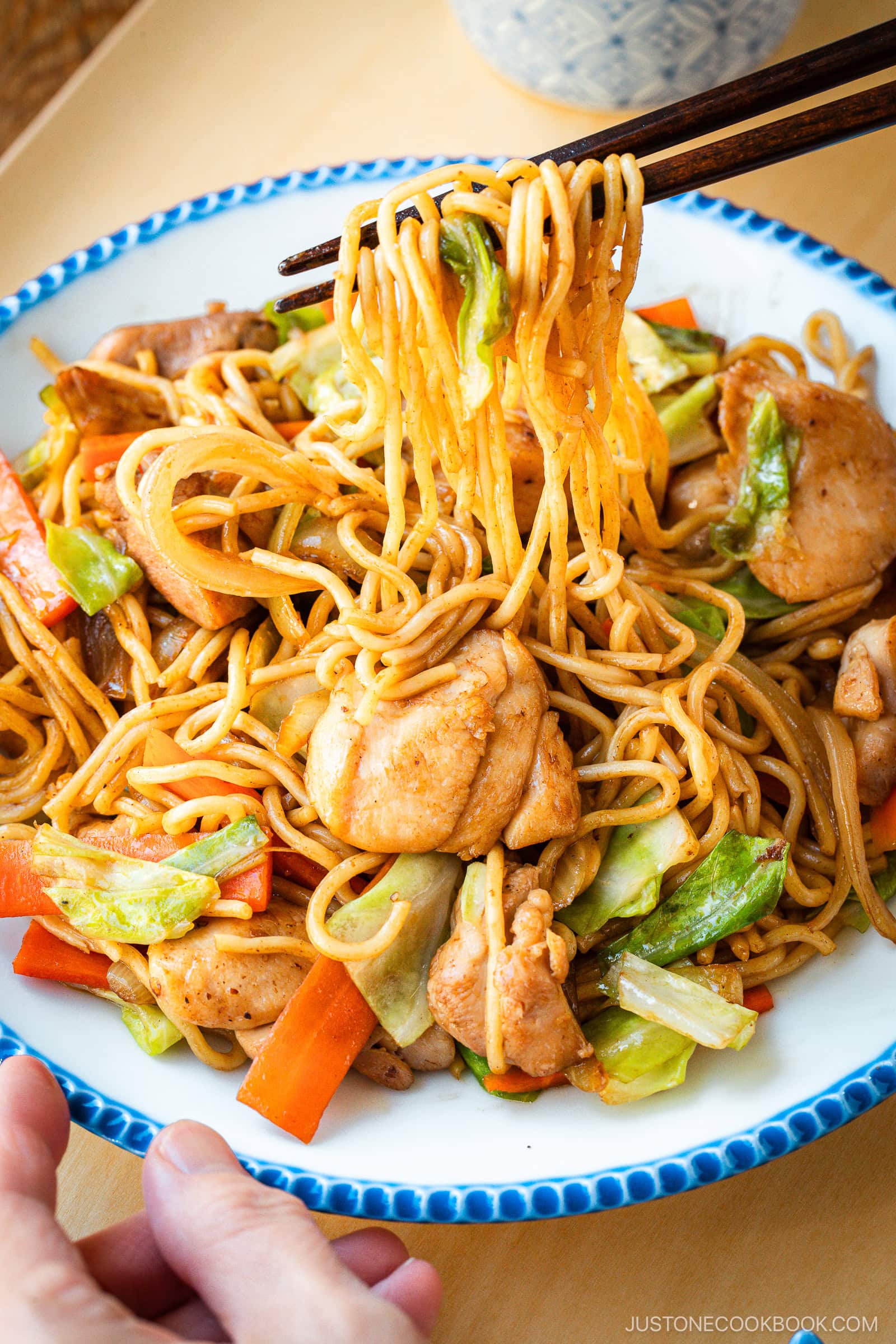 Delicious Chicken Yakisoba with tender, moist chicken thighs and crisp veggies in a sweet savory sauce plated on a beautiful white plate with blue scalloped edge.