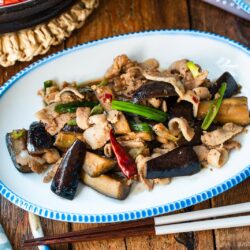 An oval plate with scalloped edge containing Pork and Eggplant Stir Fry served with multigrain rice and miso soup.