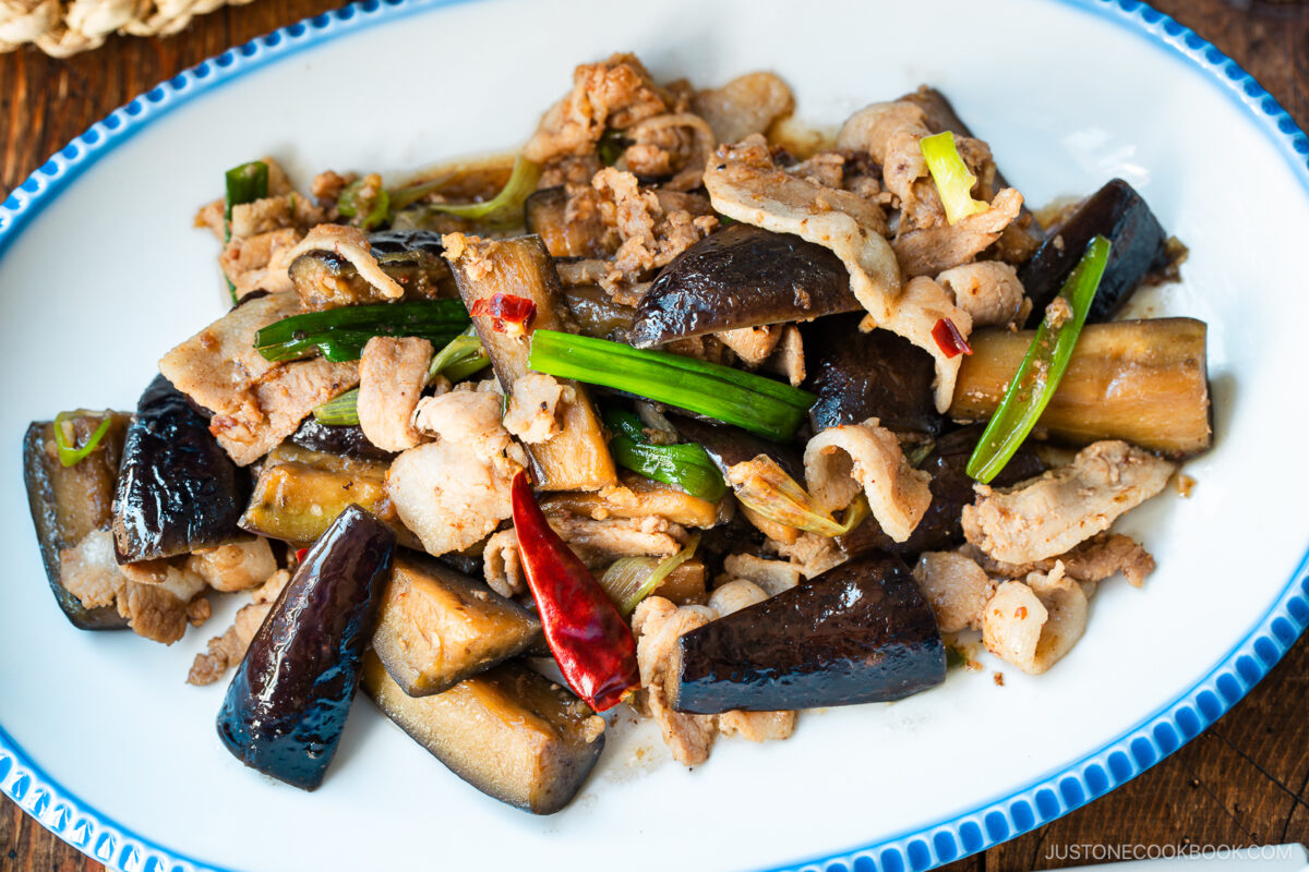 An oval plate with scalloped edge containing Pork and Eggplant Stir Fry served with multigrain rice.