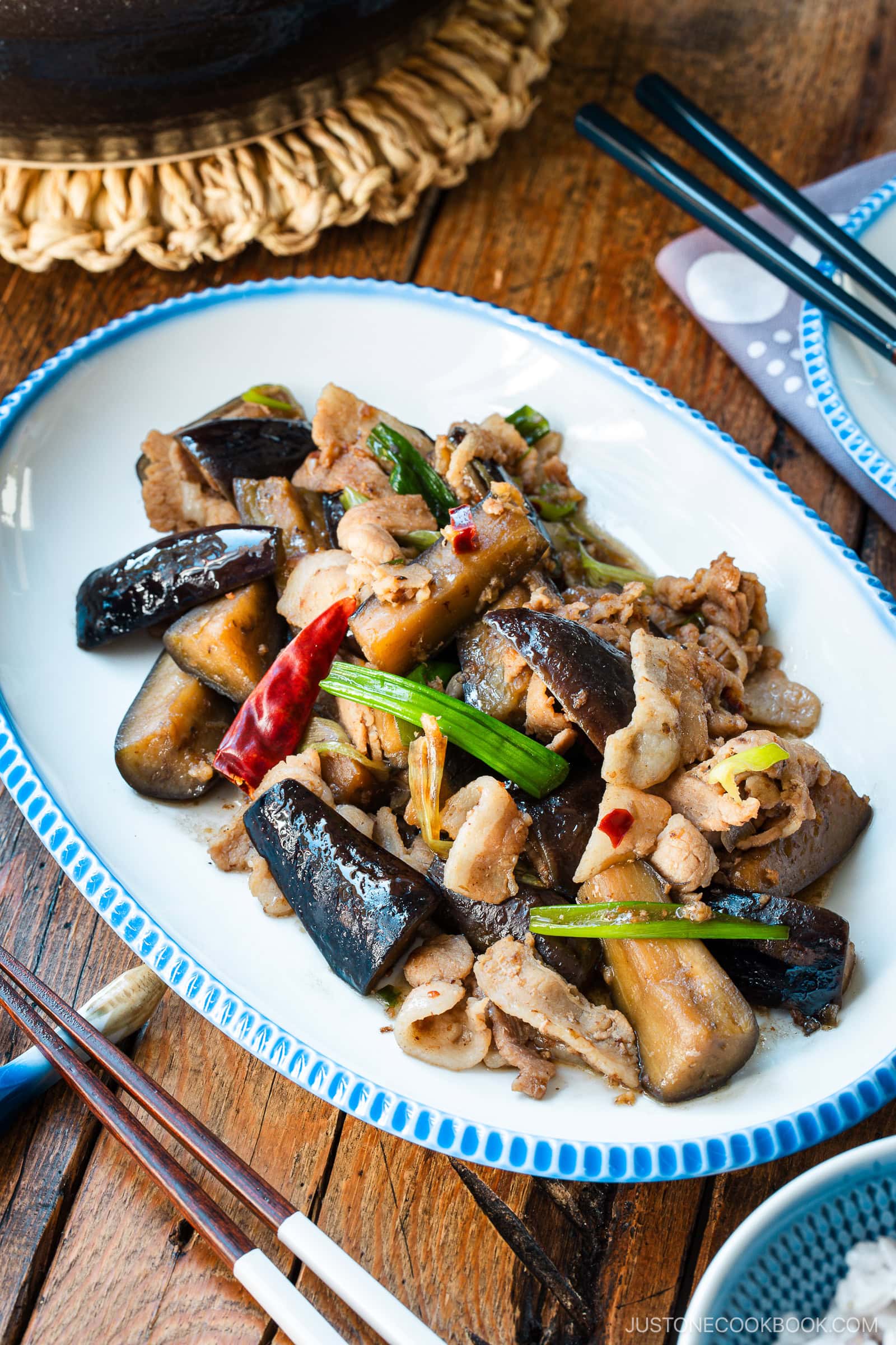 An oval plate with scalloped edge containing Pork and Eggplant Stir Fry served with multigrain rice.