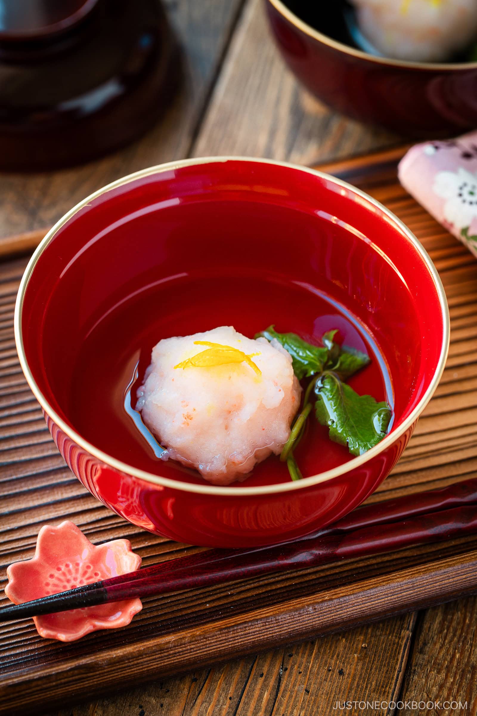 Fluffy Japanese yudofu, delicate tofu ball with garnish in a red bowl, traditional Japanese cuisine served with fresh herbs on a wooden tray.
