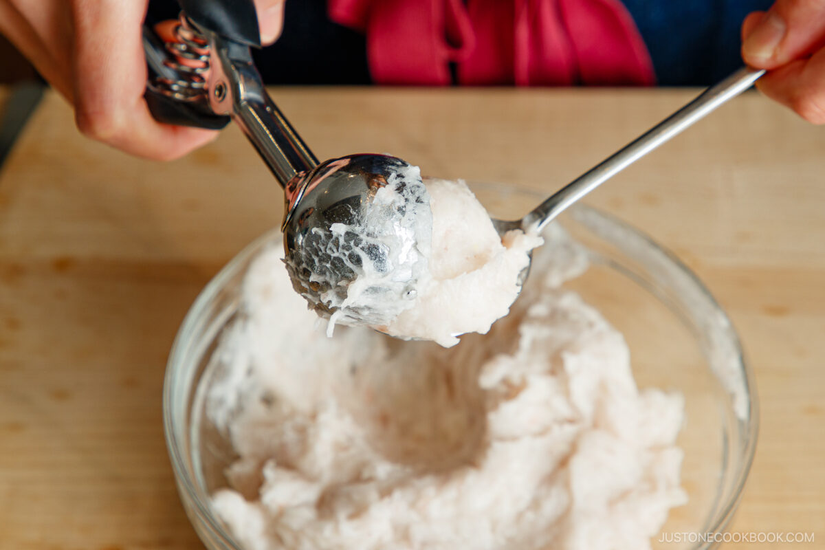 Transferring a cookie scooper filled with shrimp paste into a tablespoon.