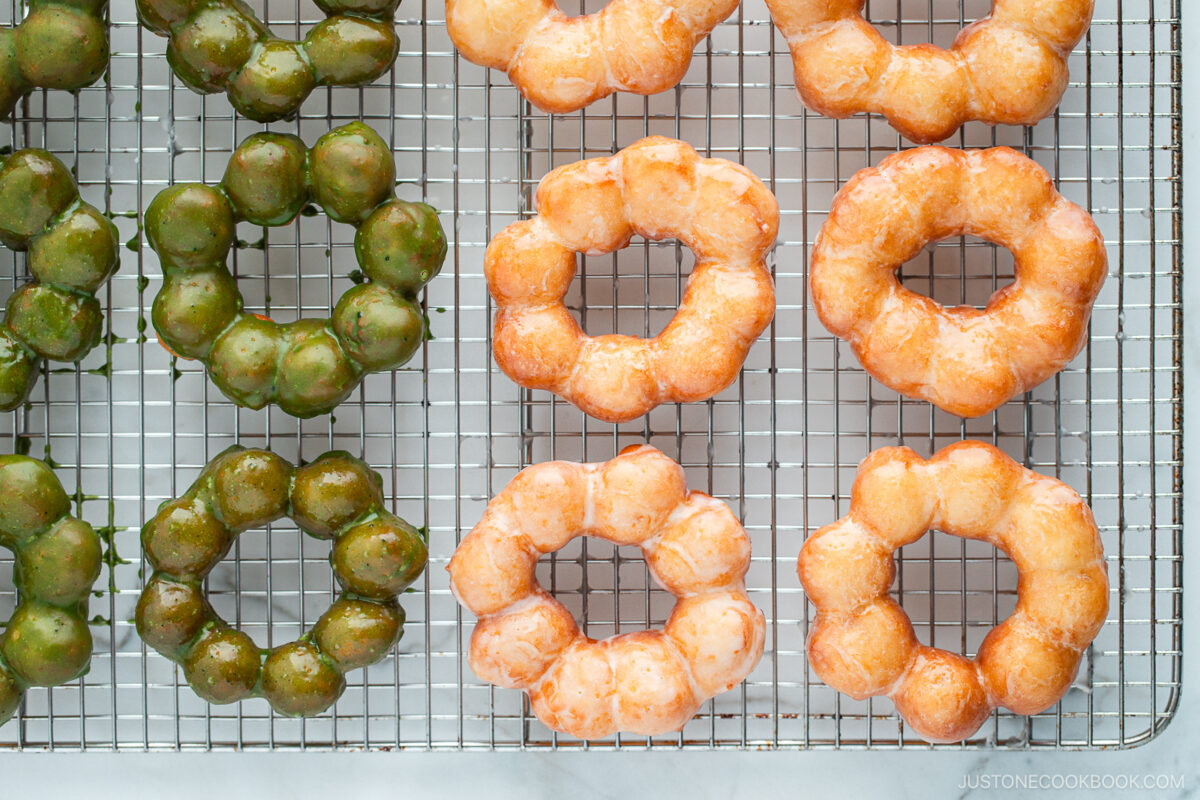 Copycat Pon de Ring donuts, hot from the fryer and still glistening with sugar and matcha glaze, cooling on a wire rack.
