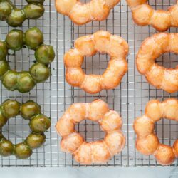 Copycat Pon de Ring donuts, hot from the fryer and still glistening with sugar and matcha glaze, cooling on a wire rack.