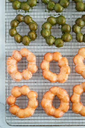 Copycat Pon de Ring donuts, hot from the fryer and still glistening with sugar and matcha glaze, cooling on a wire rack.