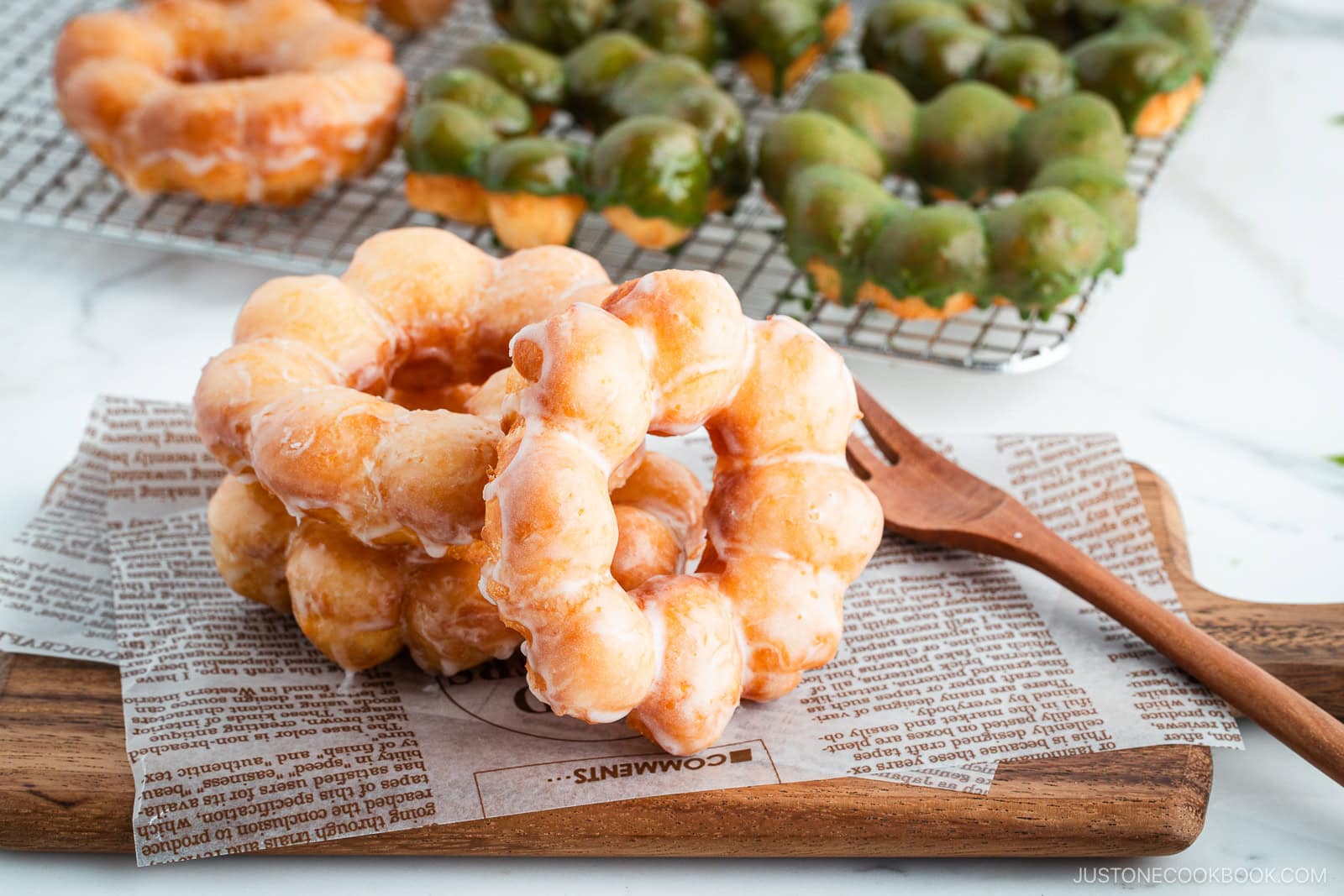 Copycat Pon de Ring donuts, hot from the fryer and still glistening with sugar and matcha glaze, stacked atop one another on a rustic wooden board.