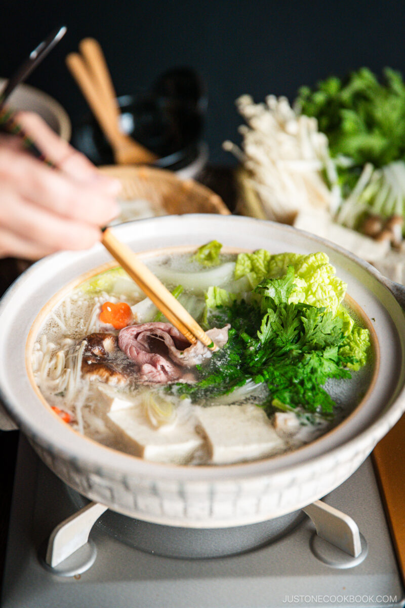 Thinly sliced beef is being cooked in the hot pot along with vegetables and tofu in a donabe, Japnaese hot pot.