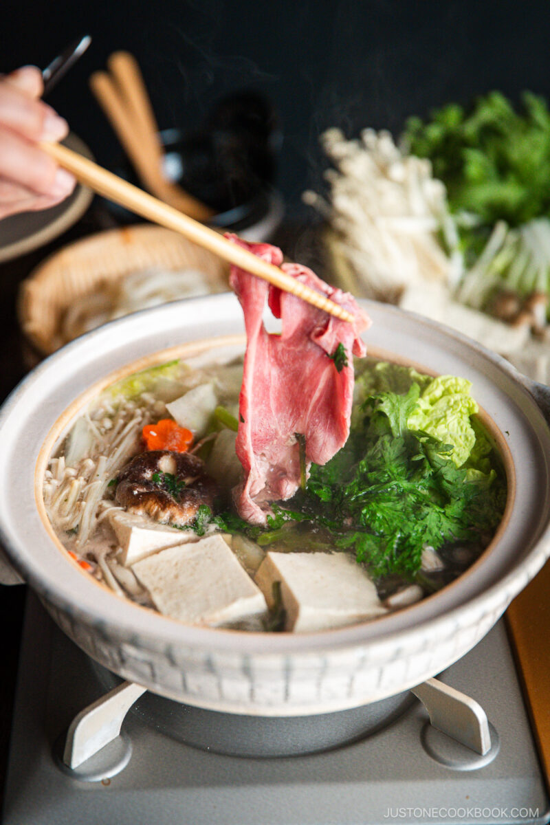 Thinly sliced beef is being cooked in the hot pot along with vegetables and tofu in a donabe, Japnaese hot pot.